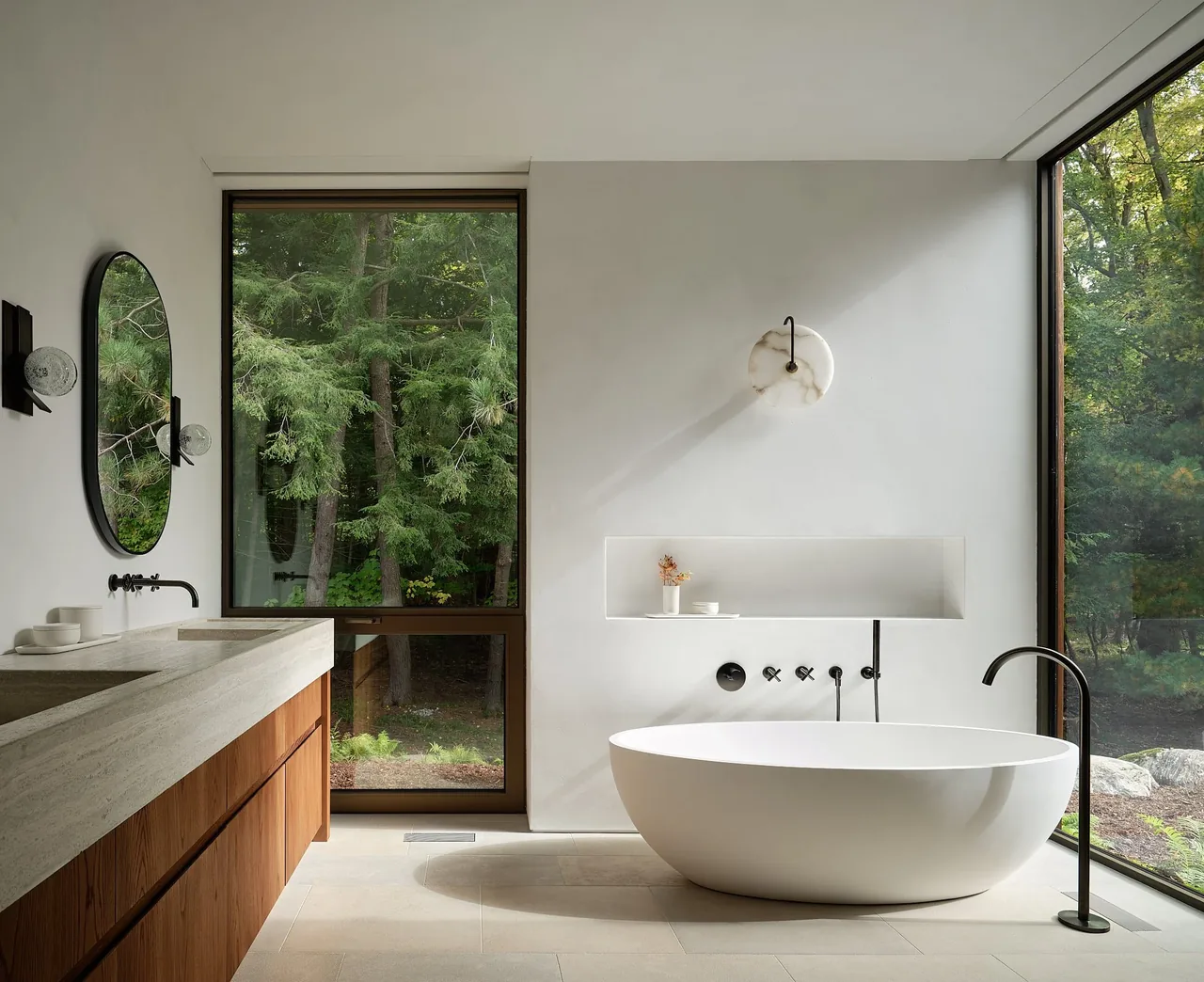 A modern bathroom featuring a freestanding oval tub and large glazing overlooking trees.
