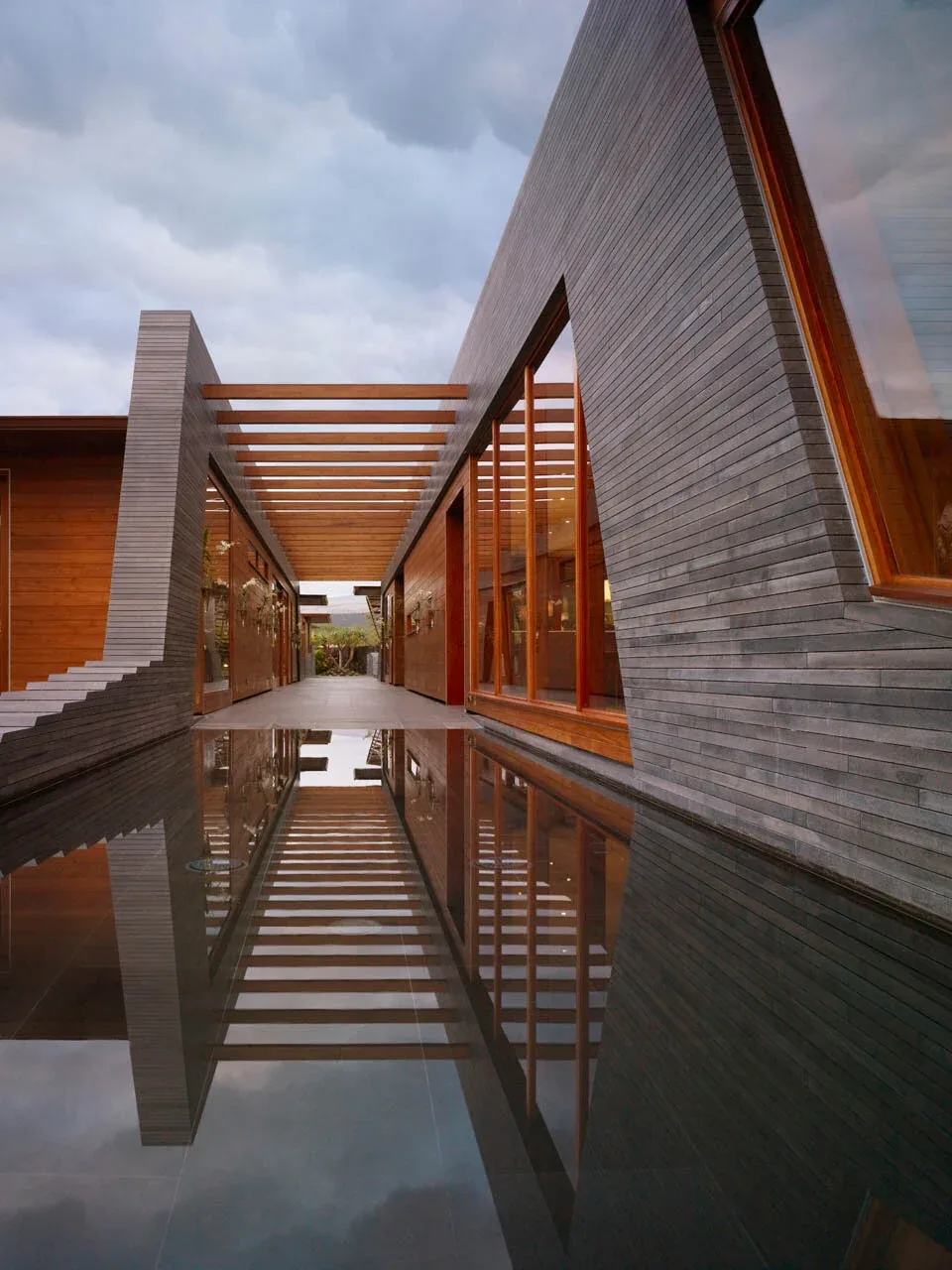 Narrow exterior corridor with wood and concrete materials reflecting in a shallow pool