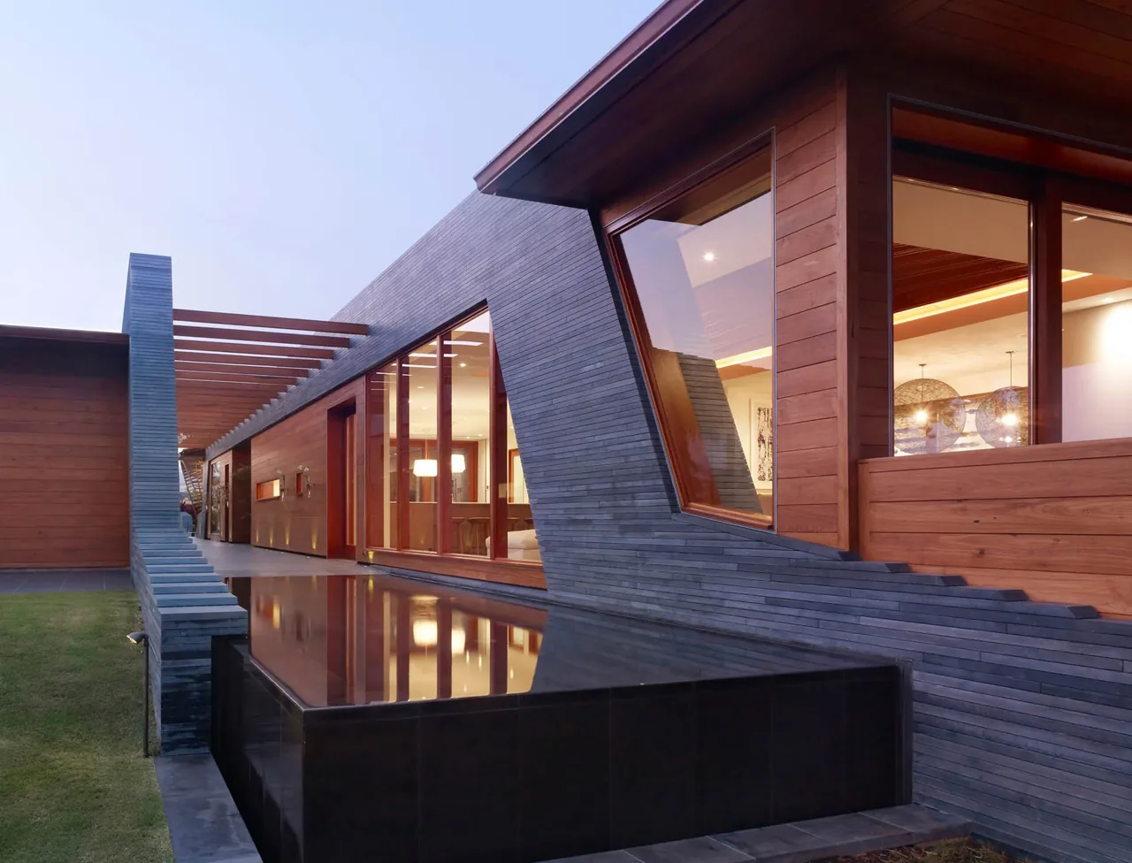 Exterior view of Kona Residence featuring wood siding, large wood-framed windows, and a reflective water feature.