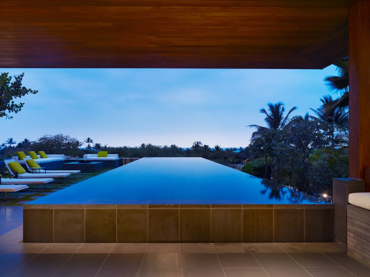 Infinity pool with lounge seating area, surrounded by landscape and sky at dusk.