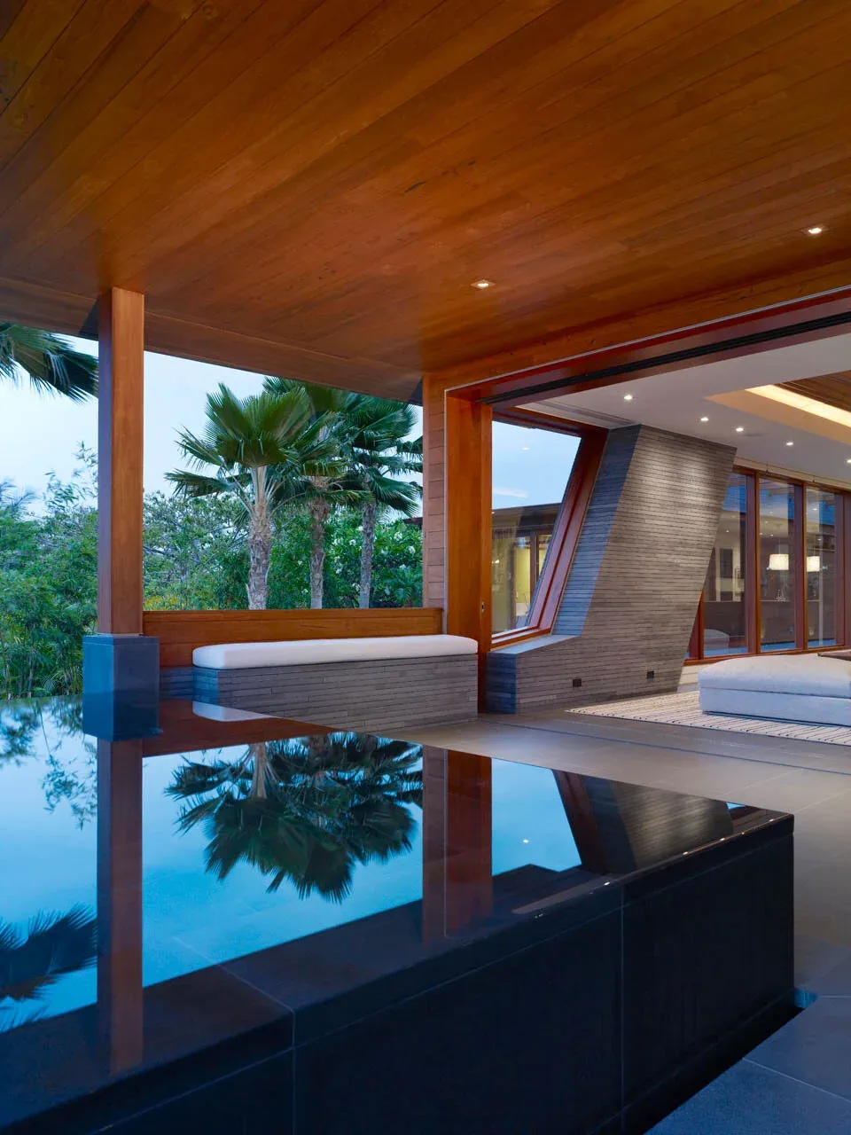 Covered patio area with wood cladding, built-in bench, and an outdoor reflecting pool at twilight.