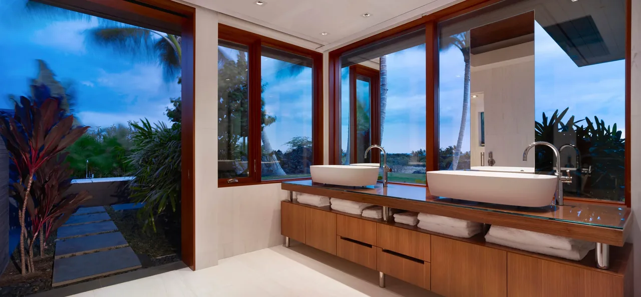 Bathroom featuring dual vessel sinks on wood countertop with large wood-framed glass windows and sliding door overlooking landscaped courtyard.