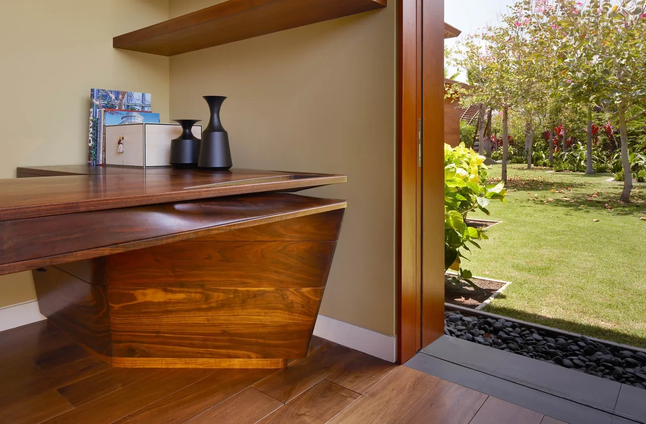 Wooden desk with angled design placed near an open door that connects interior space to a garden outdoors.