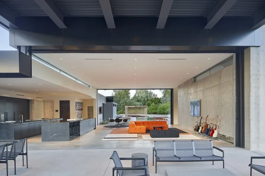 Living room with concrete walls, orange sofa, and large sliding glass doors opening to an outdoor patio with mountain views at Camelback Residence.