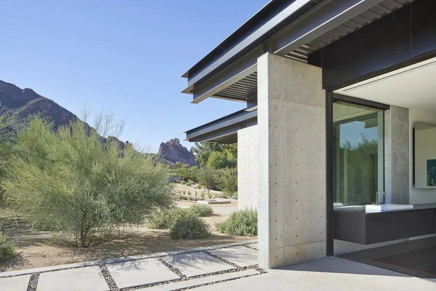 Concrete and steel exterior detail with sliding glass door opening to desert vegetation and mountain views at Camelback Residence.