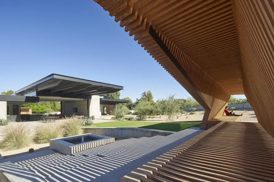 The Camelback Residence features a distinctive wooden slat structure shading an outdoor seating area with a sunken concrete patio in the desert landscape.