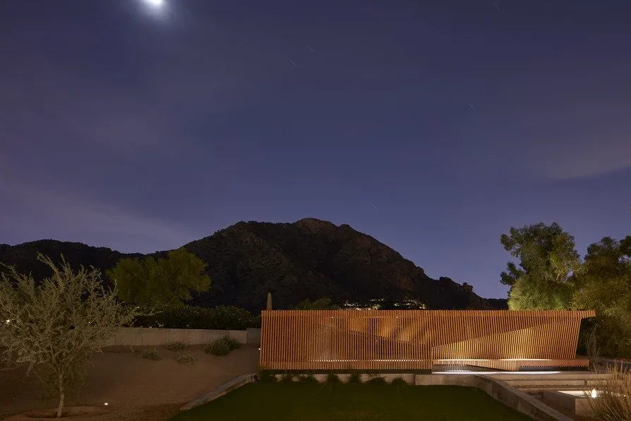 Camelback Residence backyard with a wooden slat fence and desert landscape visible under the moonlight.