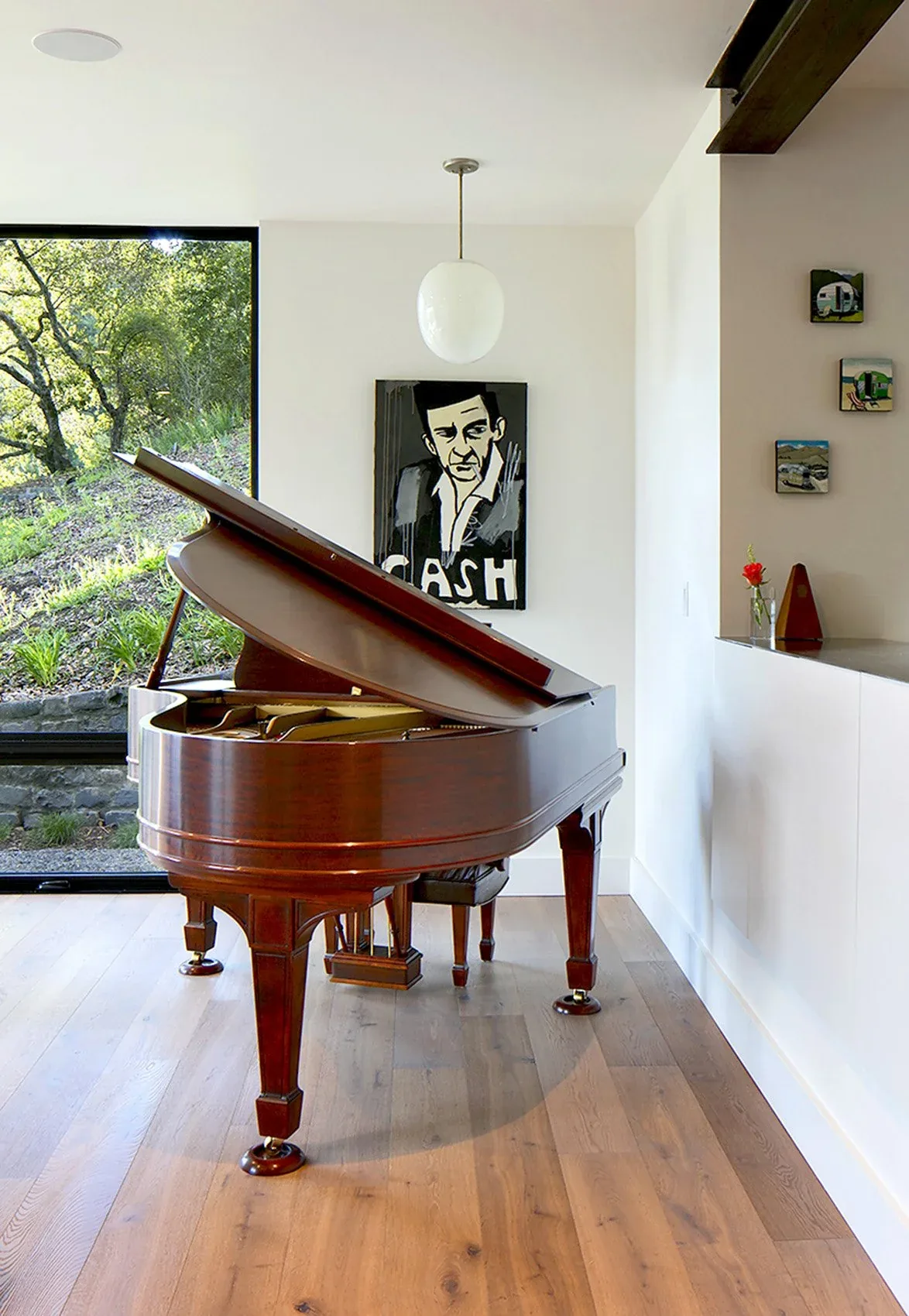 An elegant grand piano sits near a floor-to-ceiling window in a modern living space with wood flooring.