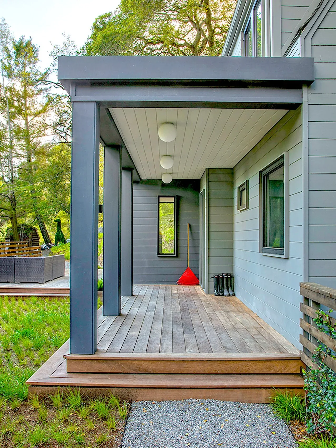 The covered porch features gray wood siding, a white paneled ceiling with globe pendant lights, and wood decking steps outside the entrance.