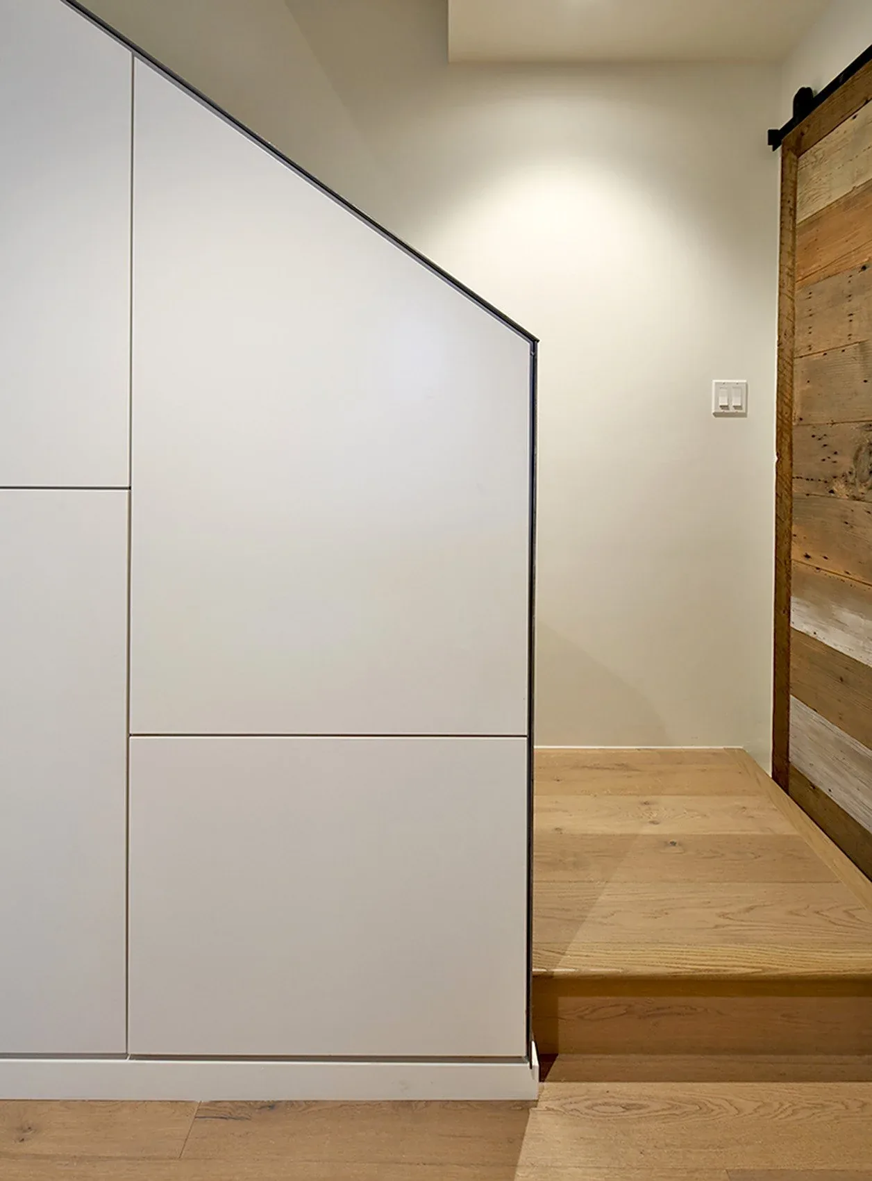 Modern stair section with white panel wall and rustic wooden sliding door adjacent to light oak flooring.