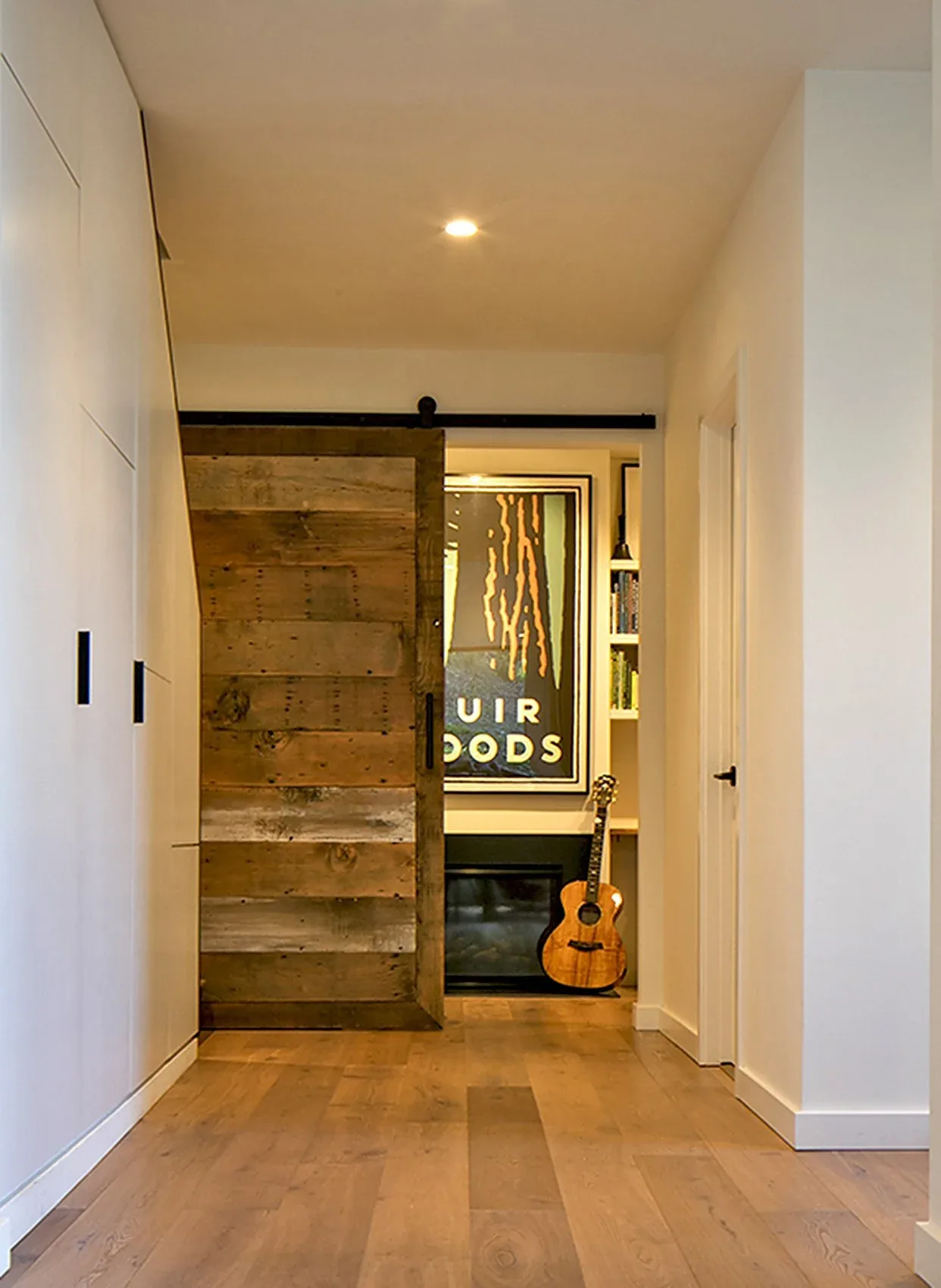 Interior hallway featuring a sliding barn door made of rustic wood planks and a view into a room with a guitar and framed art.