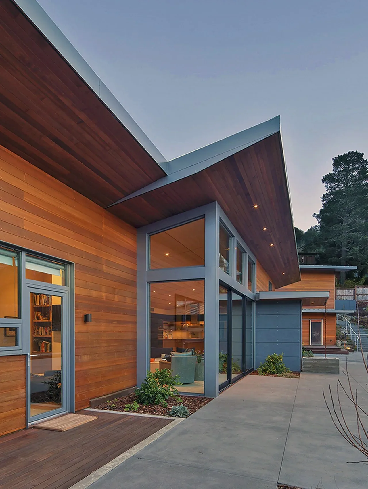 Modern house exterior featuring wood siding, large gray-framed corner windows, and an angled roof with wood paneling under the eaves.