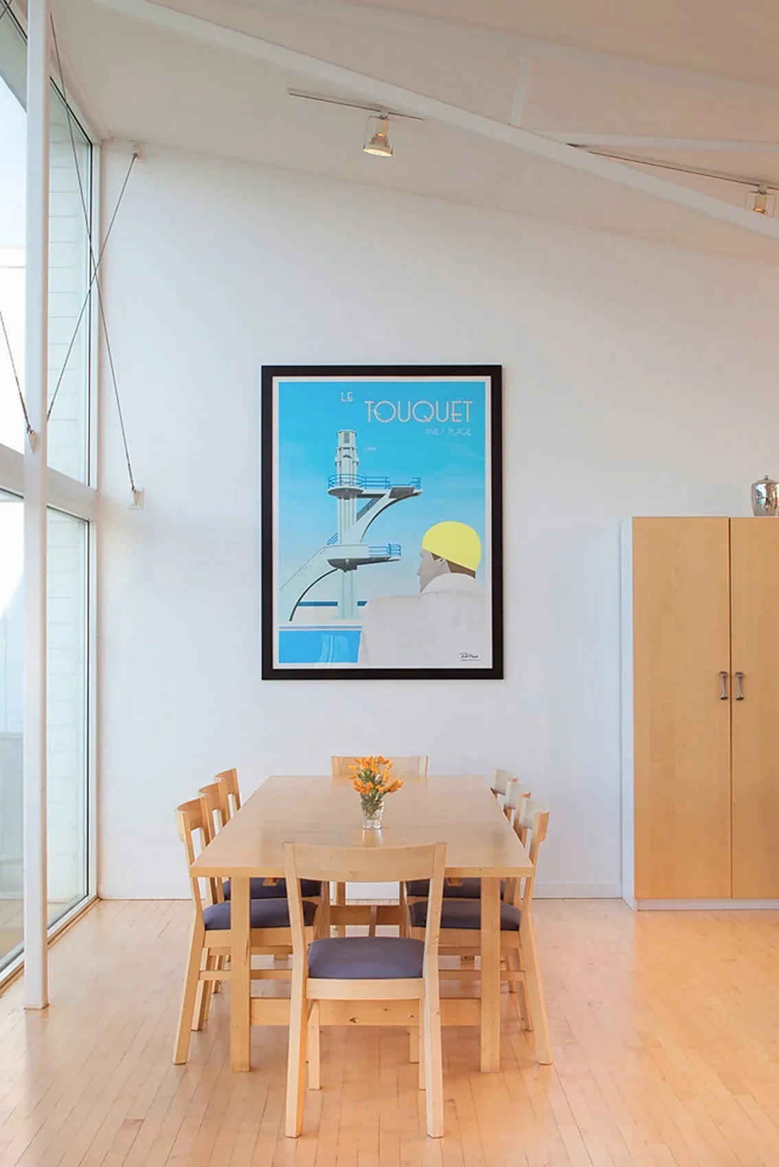 Minimalist dining space with light wood furniture and a framed poster on the wall.