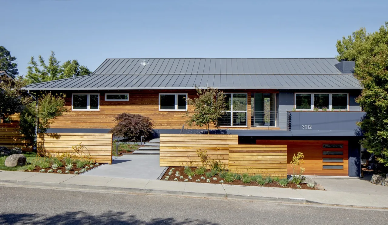Modern house front with metal roof, horizontal wood fencing, and landscaped yard with concrete steps.
