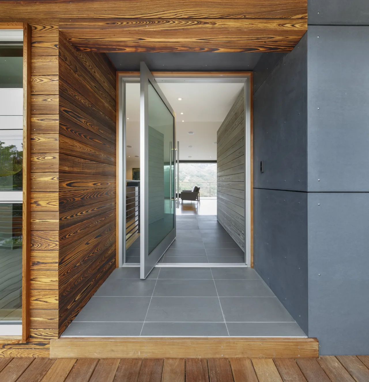 Entryway shows a glass pivot door opening into a hallway with wood siding and gray tile flooring inside.