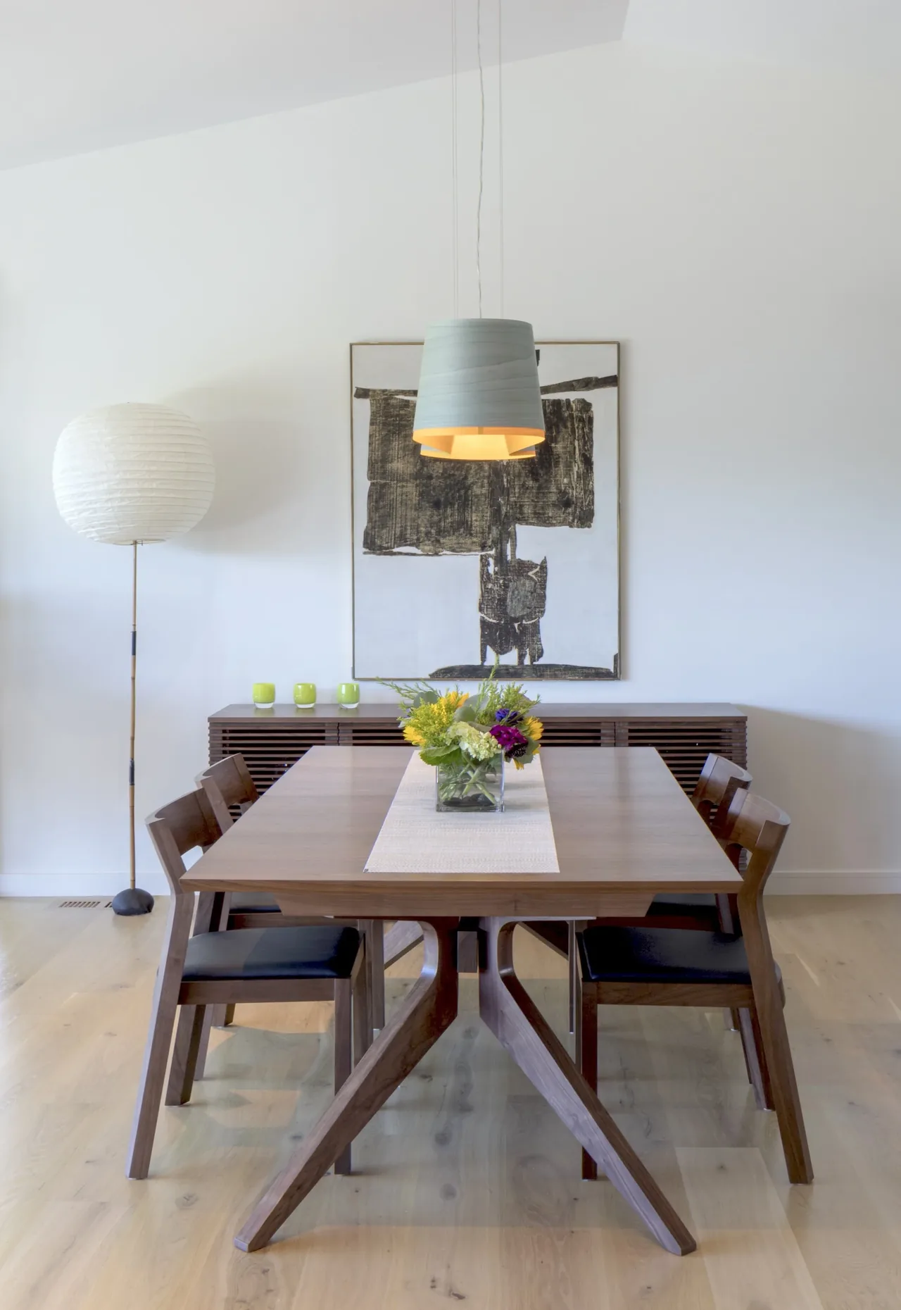 Dining area featuring a wooden table with modern chairs under a pendant light and abstract wall art.