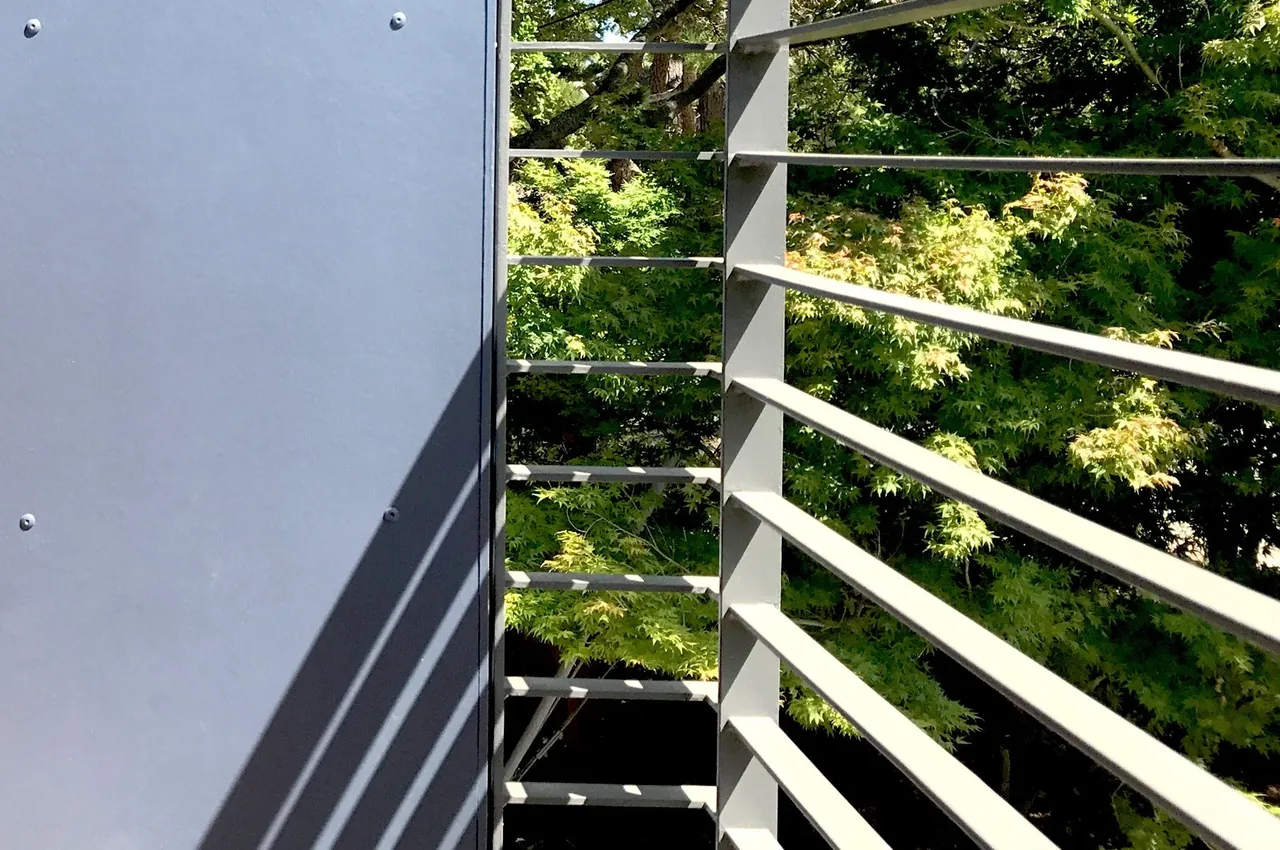 Gray horizontal metal railing detail with green trees visible in the background.