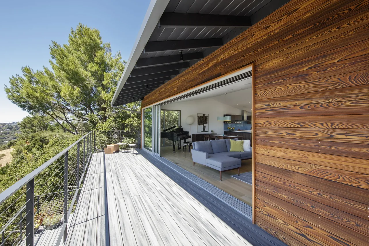 Open balcony with metal horizontal railing and wood siding exterior leading into a living space with gray upholstery and grand piano.