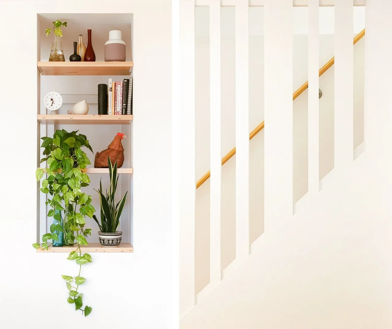 Wood shelves built into white wall hold plants and decor next to a staircase with a wood handrail and white vertical slats.