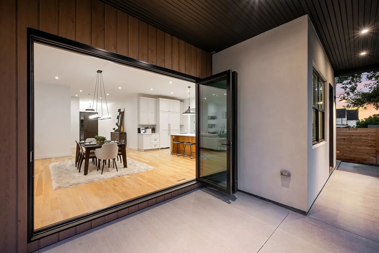 Indoor dining area and kitchen seen through open folding glass door from exterior patio at sunset.