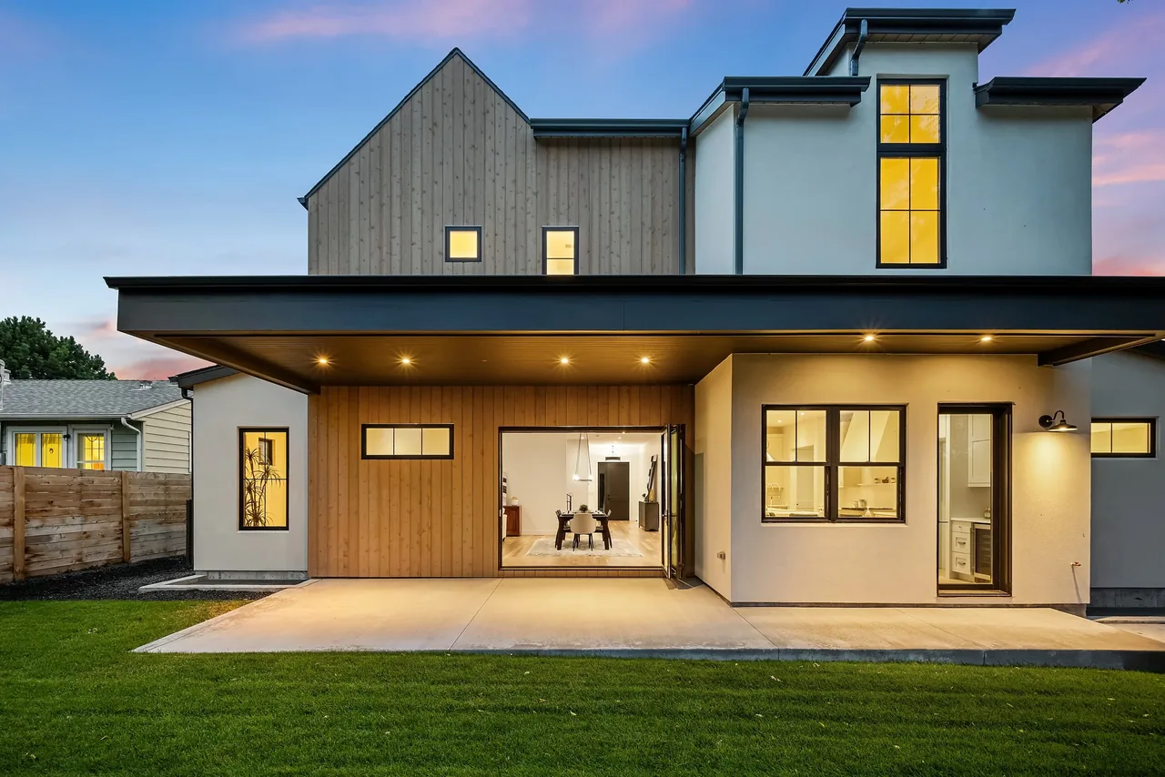 Rear exterior of a modern two-story house featuring a covered patio with recessed lighting and mixed wood siding and stucco walls.