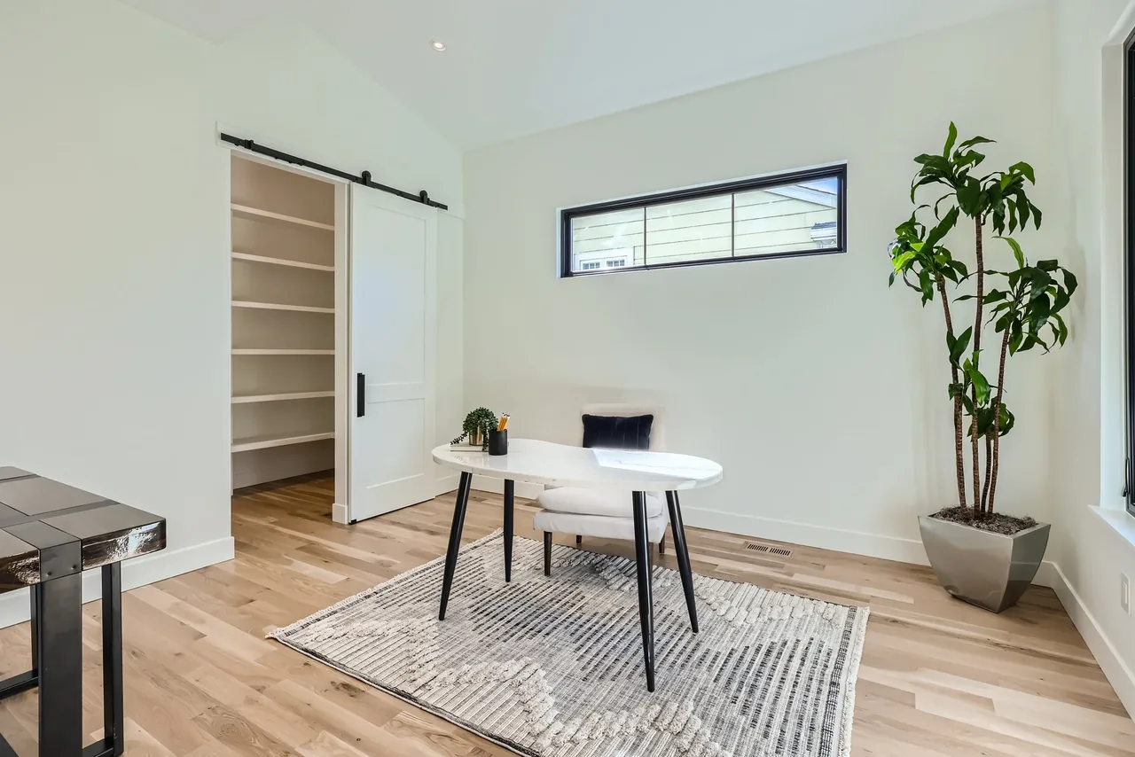 A modern office space with light wood floors, a sliding barn door, and a small white desk.
