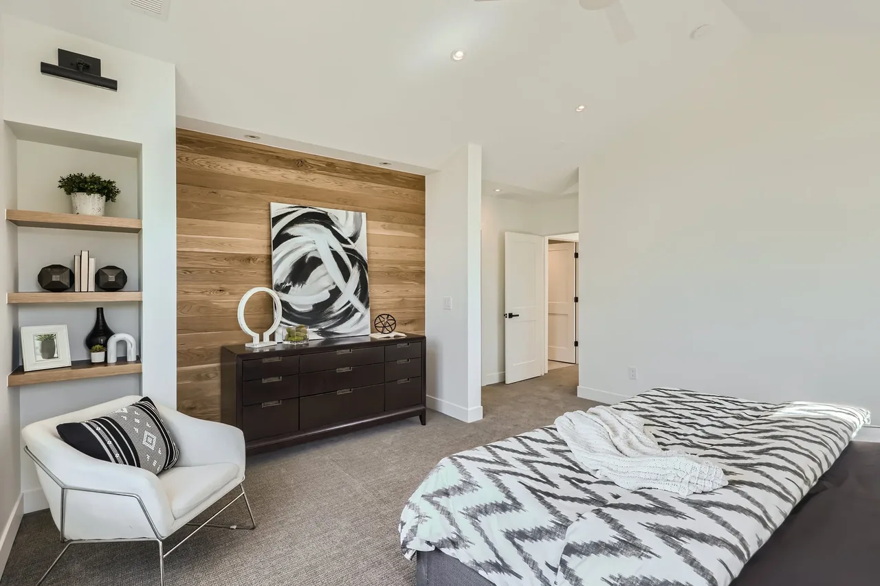 A modern bedroom featuring a wood-paneled accent wall, built-in shelves, and a white armchair.