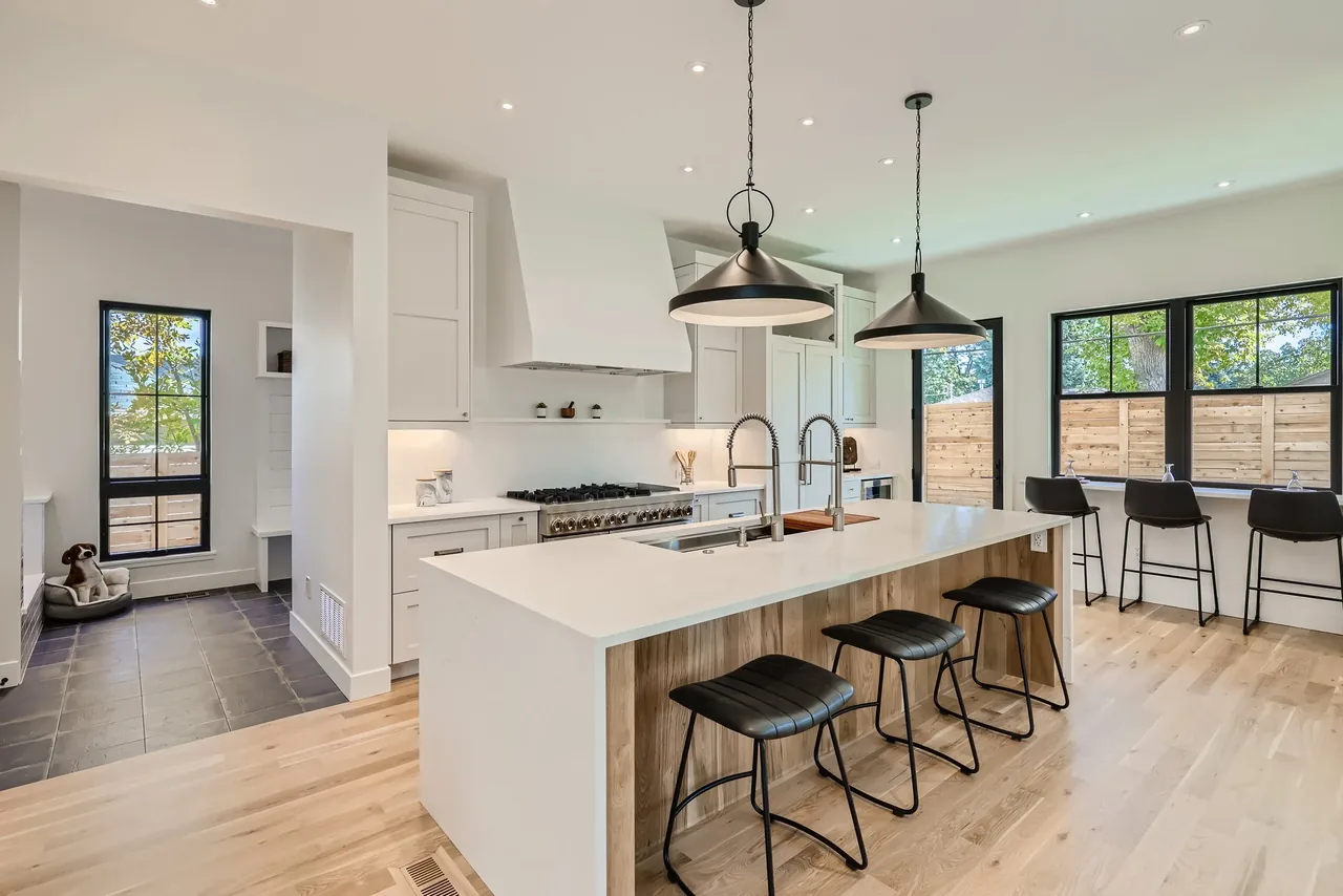 Interior view of a modern kitchen with island, pendant lighting, and black-framed windows.
