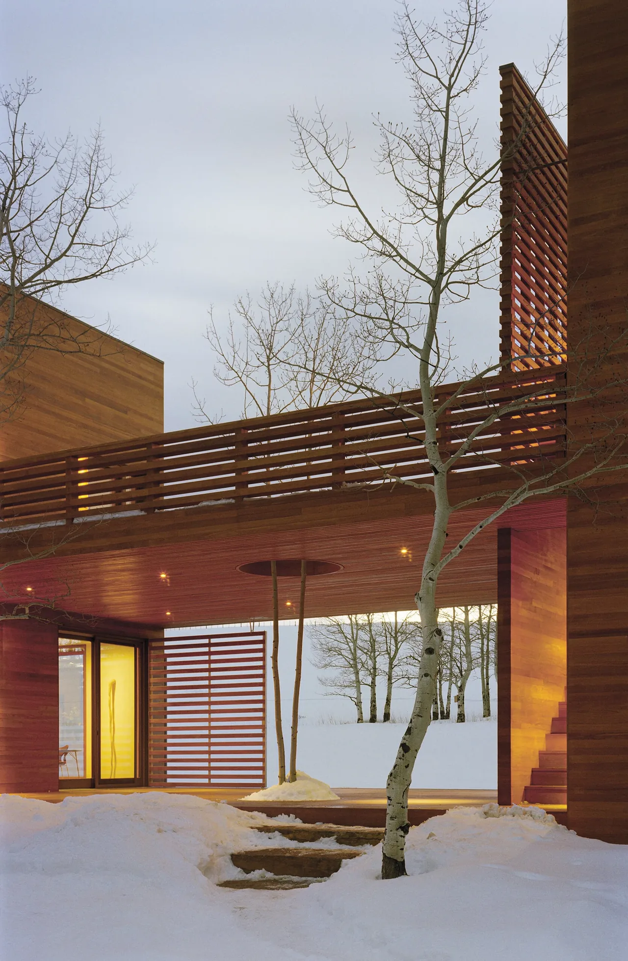 THE BOX HOUSE features a wooden exterior with a covered passage integrating natural trees and snowy surroundings.