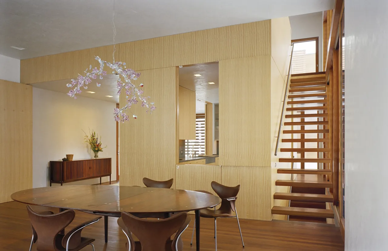 Dining area with wood table and chairs, open riser staircase, and light wood paneling.