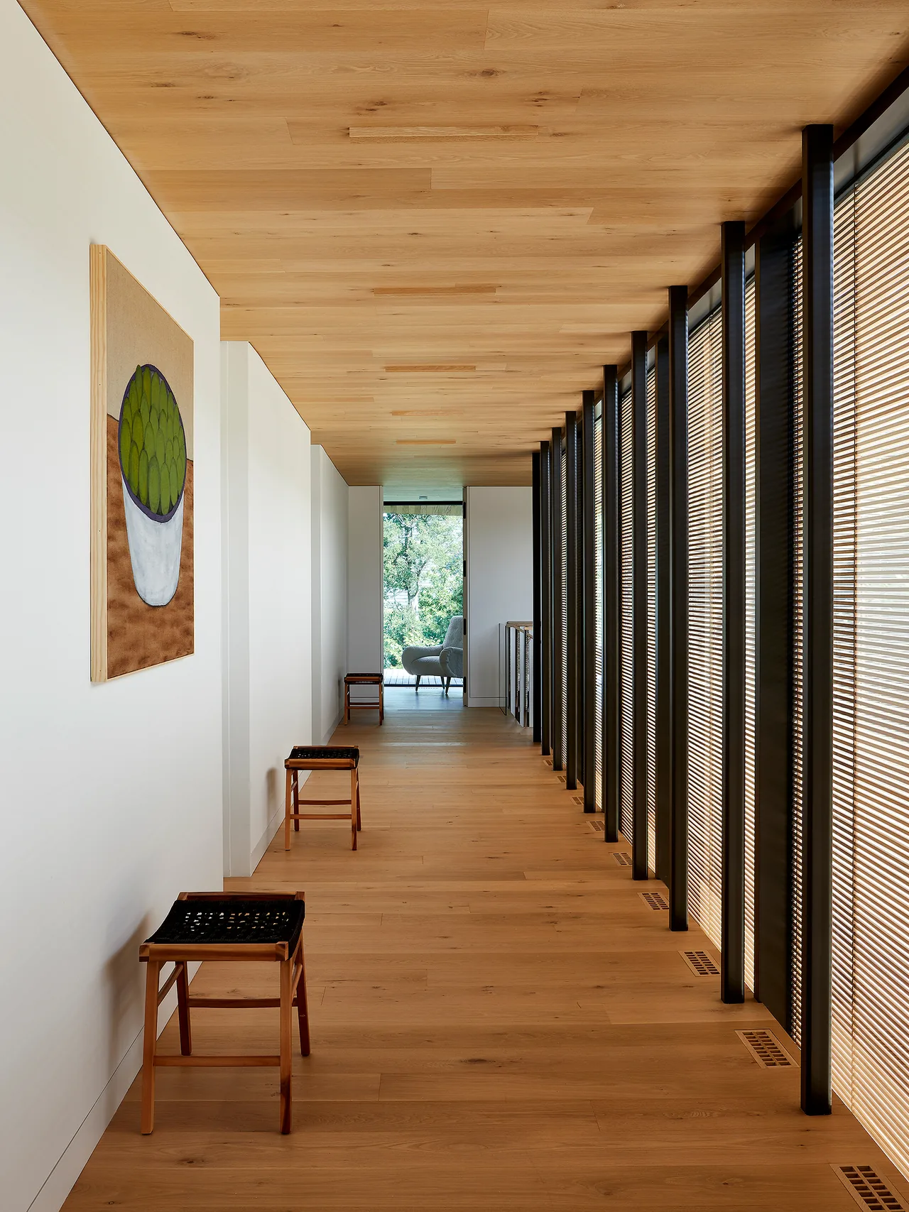 Hallway interior with wood paneling on floor and ceiling, narrow vertical windows, and minimal furniture.