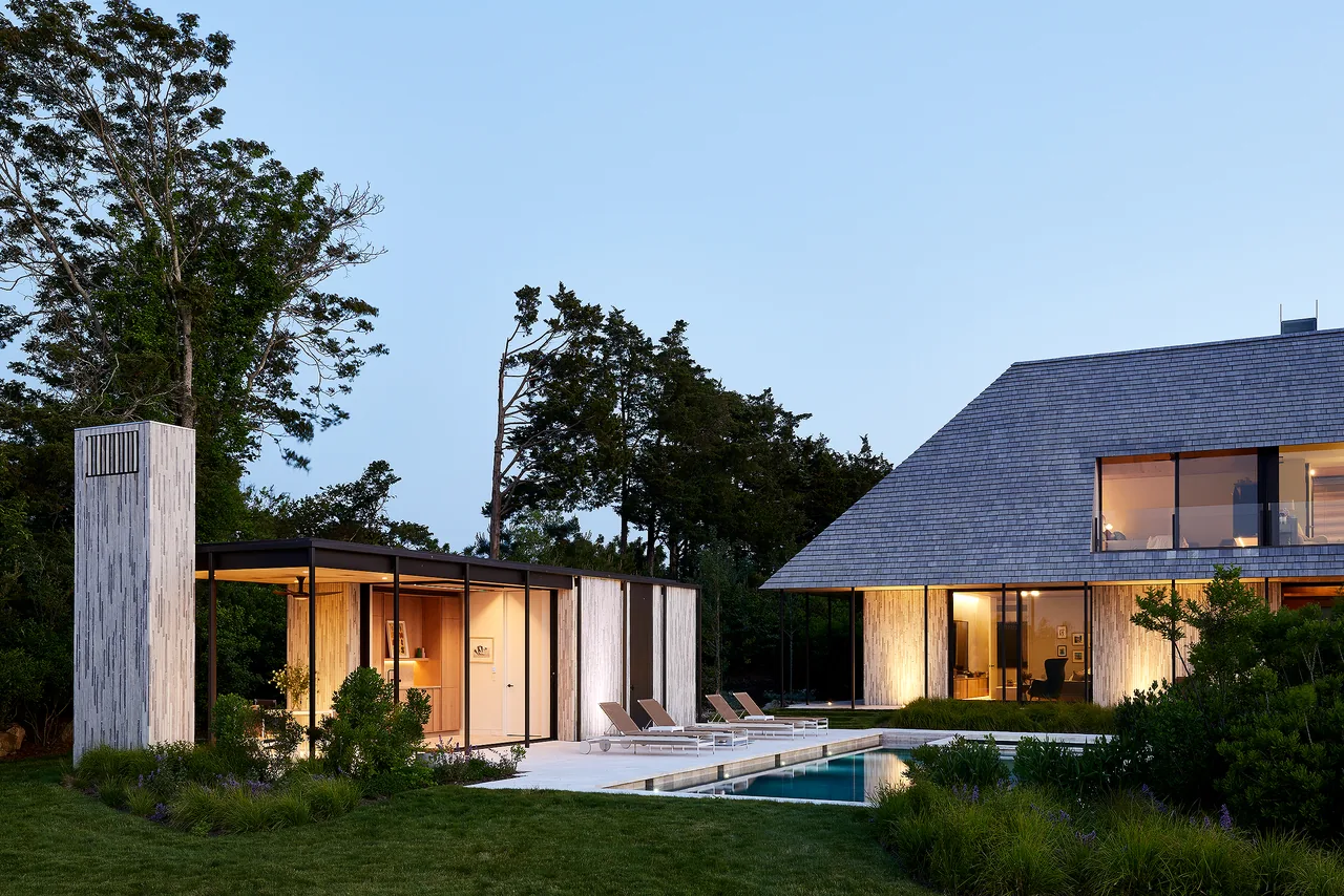 Quogue Creek project features a modern pool house and residence with a rectangular pool and lounge chairs. by Bates Masi Architects.