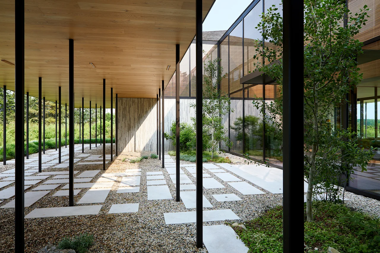 Covered patio with a wooden ceiling supported by thin black columns and a stone slab pathway over gravel leading to a garden area.