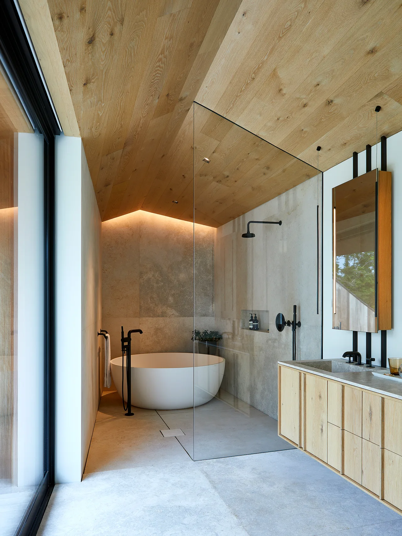 Bathroom features a wooden slanted ceiling, freestanding tub, glass-enclosed walk-in shower, and a wooden vanity with a stone countertop.