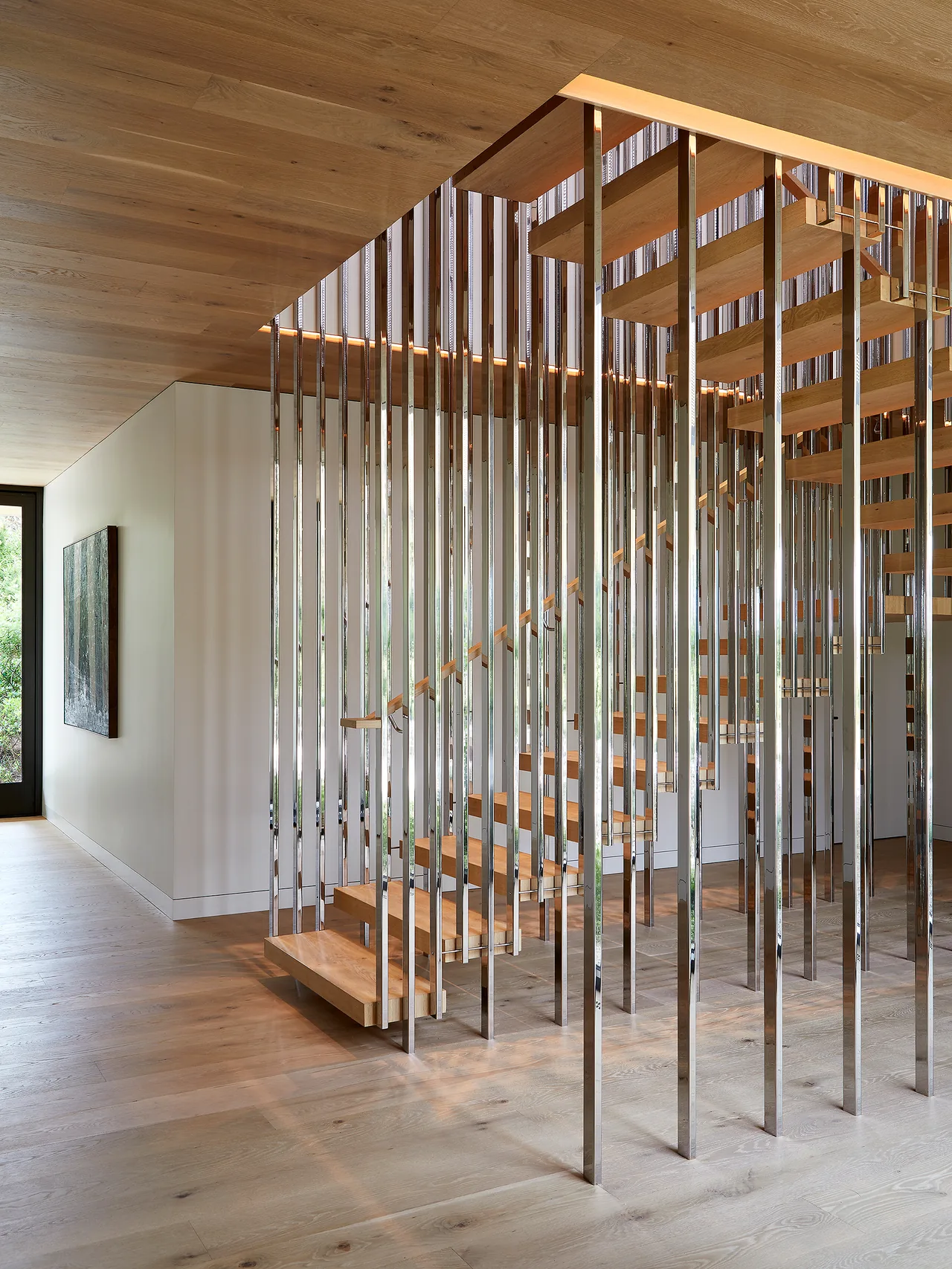 Floating wooden staircase with vertical polished metal rod supports in a modern interior.