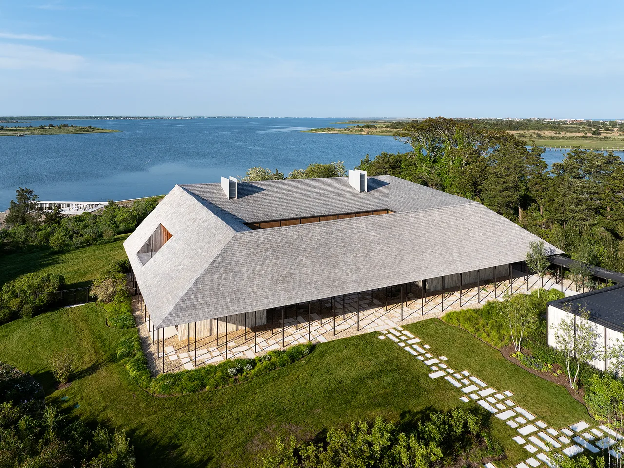 The Quogue Creek house features a hip roof with shingles and a wraparound porch supported by thin columns.