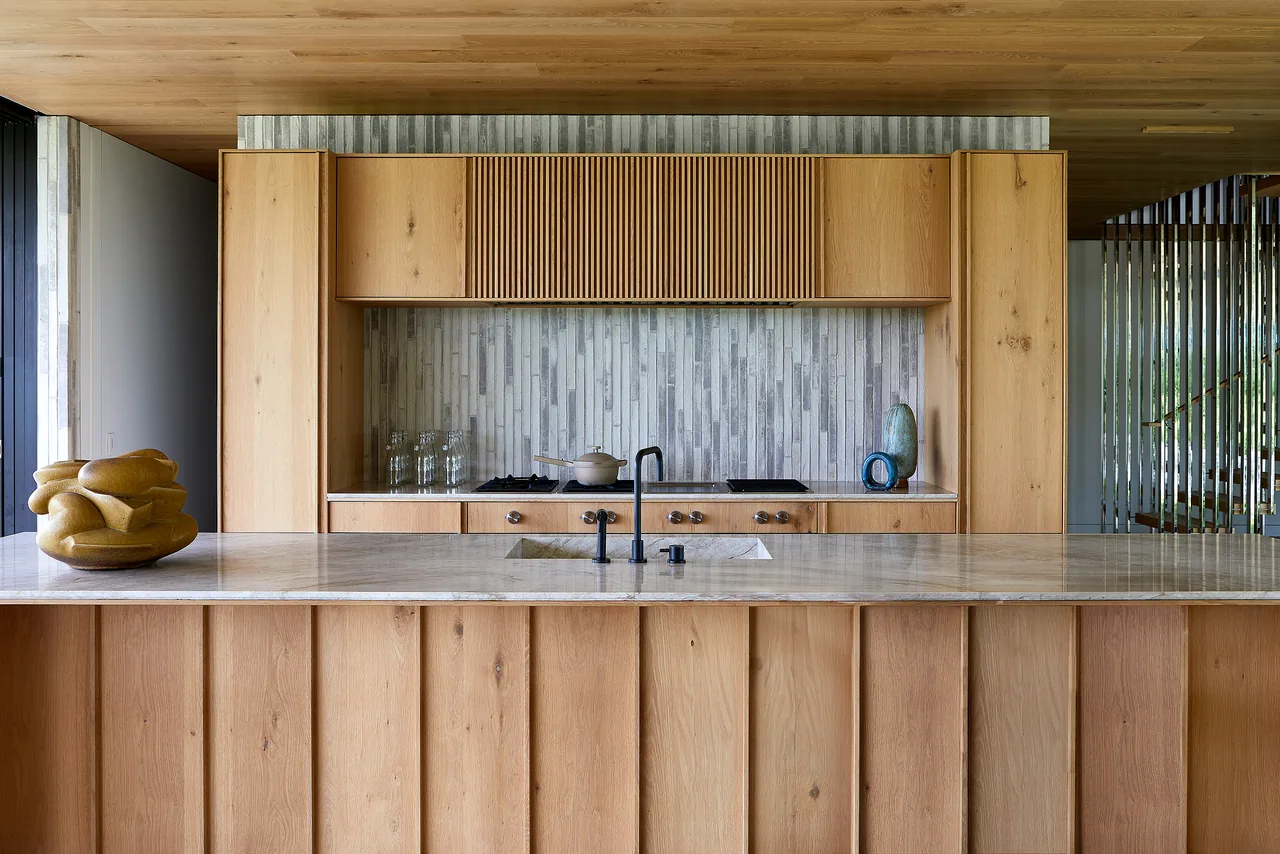 Kitchen featuring light wood cabinetry, marble countertop island, and vertical stone tile backsplash.