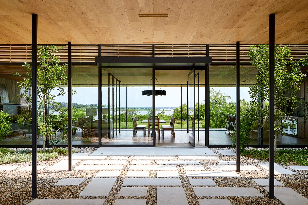 Exterior front of a modern residence with full-height glass sliding doors and a patterned stone and gravel patio.