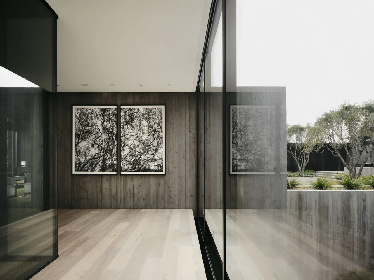 Narrow interior corridor features wood-paneled wall with black and white art and floor-to-ceiling glazing reflecting the outdoor landscape.