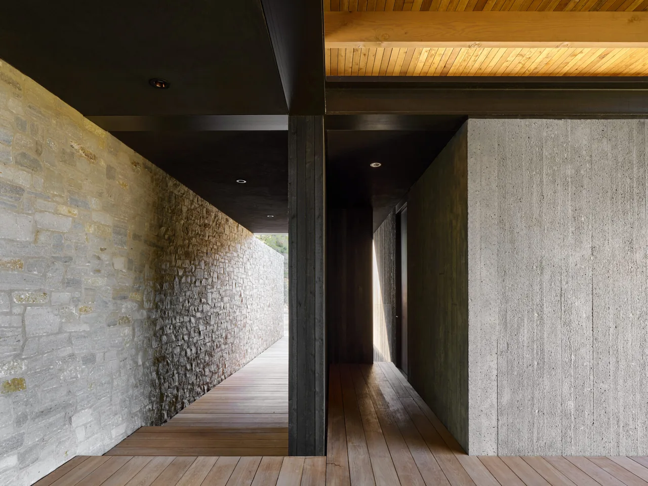 The Trestle Residence features a corridor with stone and concrete walls alongside a wood-paneled ceiling and floor.