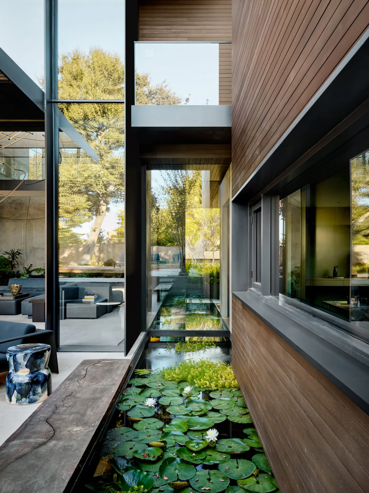 Narrow courtyard featuring a water garden between the wood-paneled residence and a glass-enclosed living area.