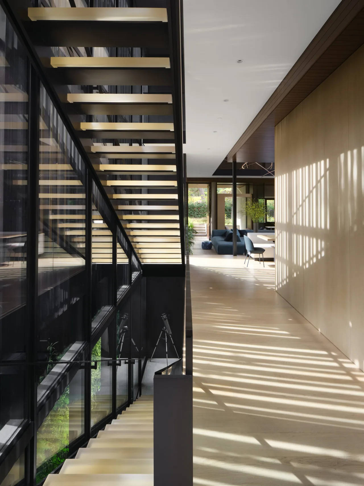 Hallway with floating staircase and black framed glass wall overlooking lower level.