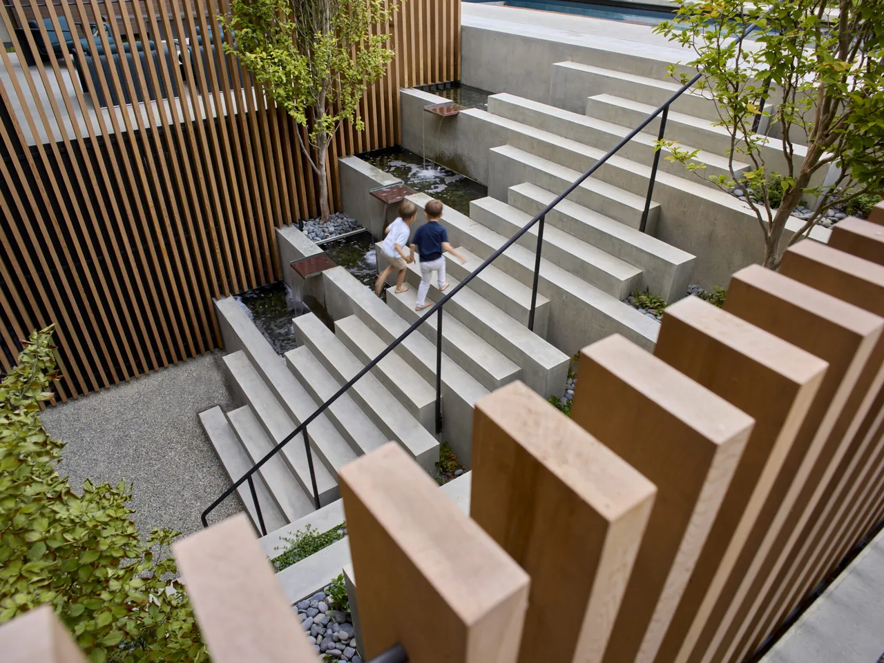 Concrete steps with adjacent water channels and wooden slat walls in a residential courtyard.