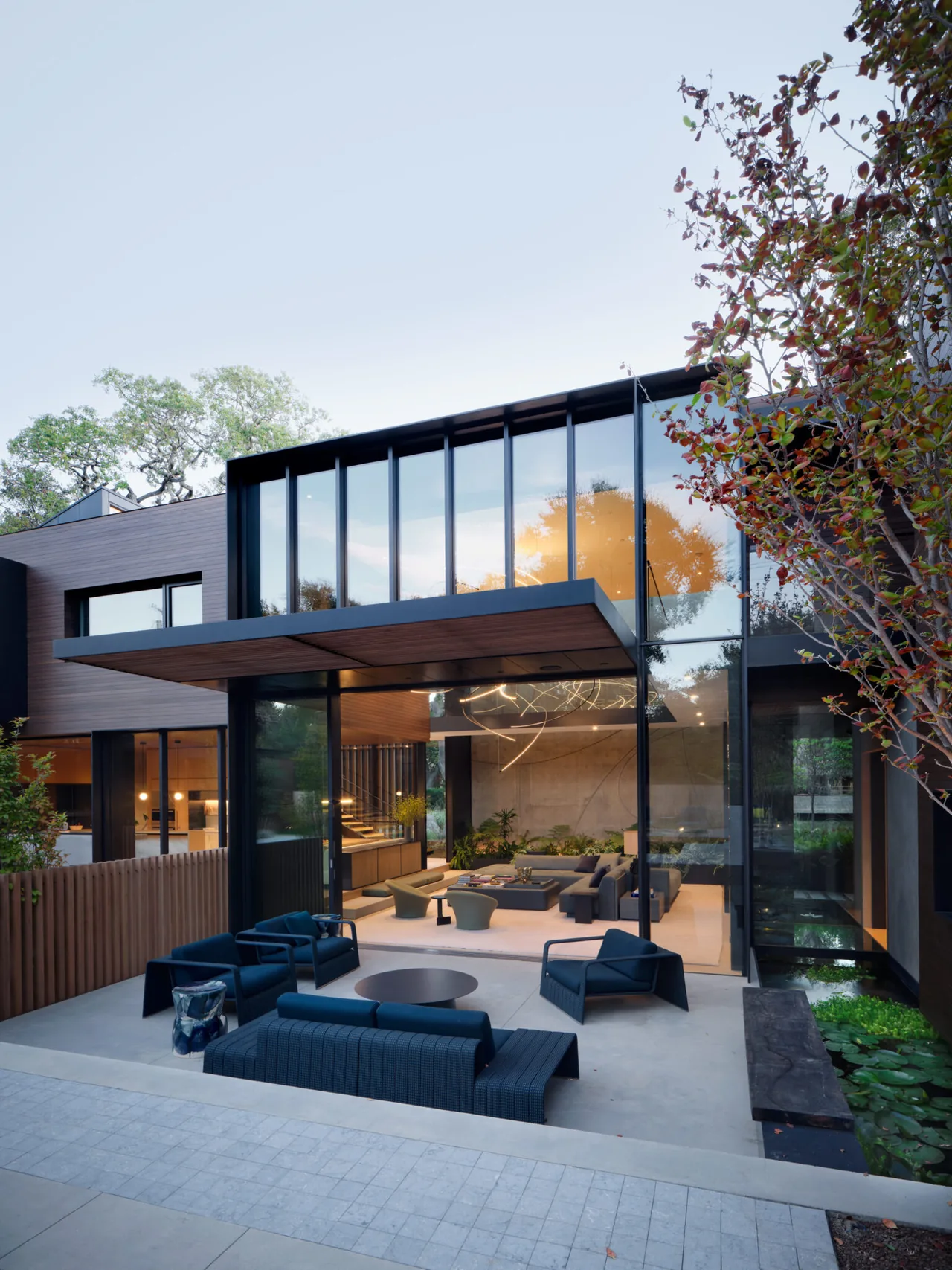 Modern residence exterior featuring a covered patio with outdoor seating and extensive glass walls.