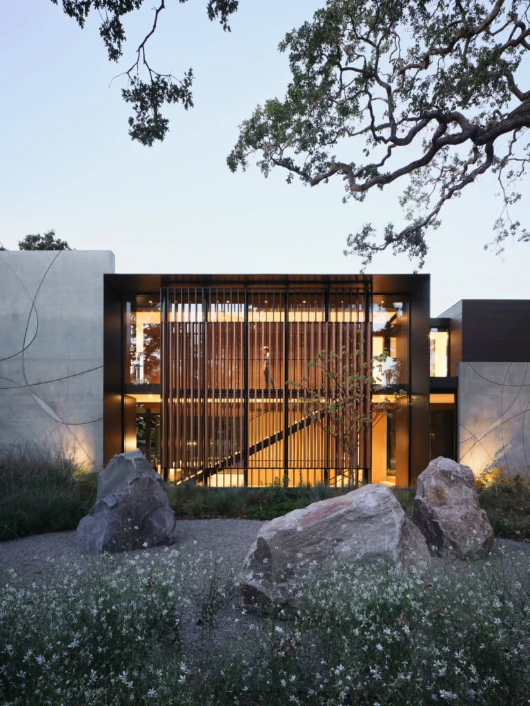 L|J Residence exterior front features vertical wood slats, glass, and concrete with integrated landscape design.