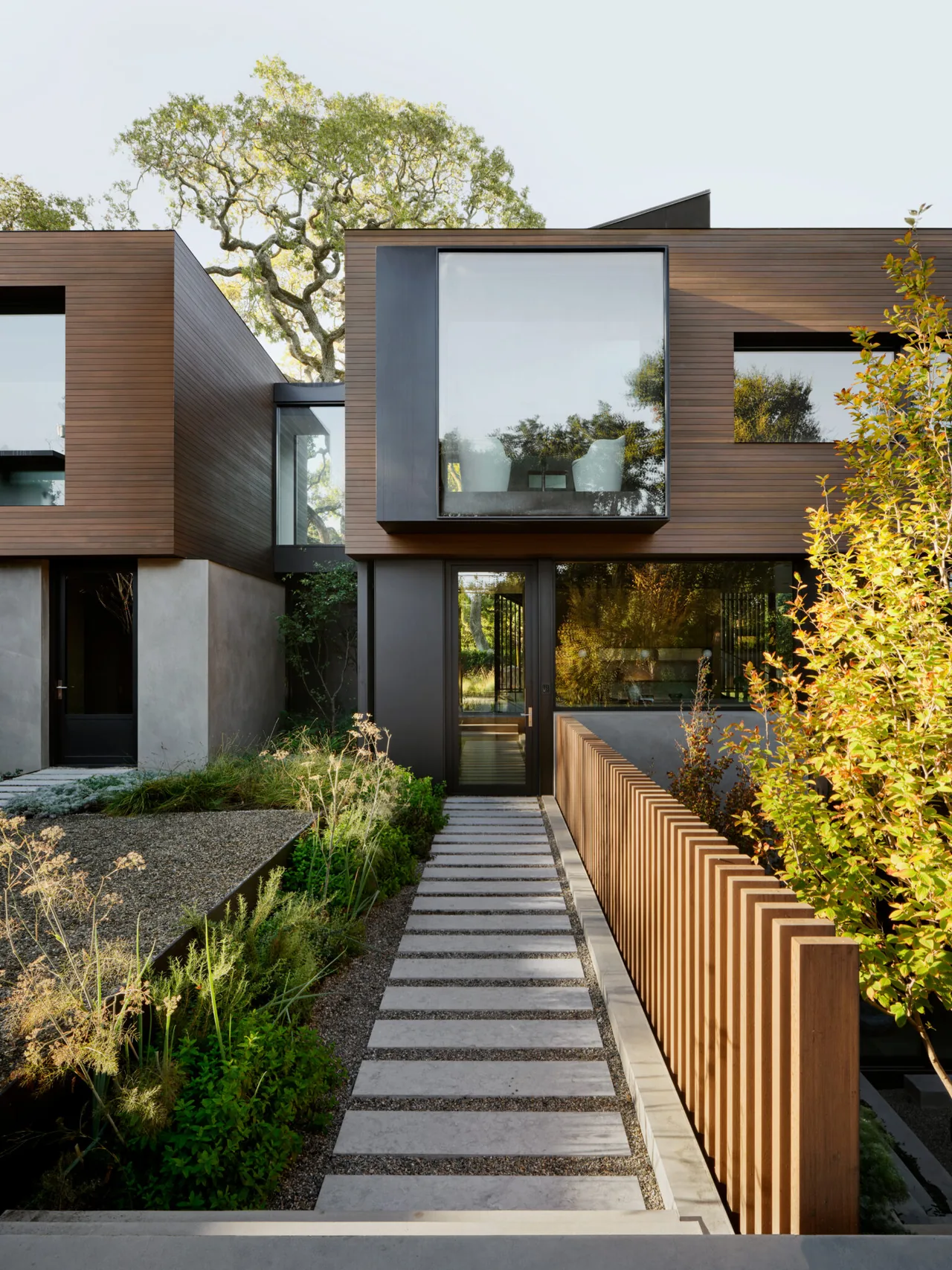 Modern exterior front view of the L|J Residence with wood siding, large windows, and a concrete walkway.