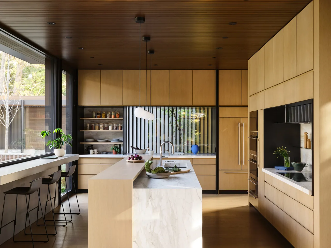 Kitchen interior featuring light wood cabinets, marble island, and large windows with garden views.