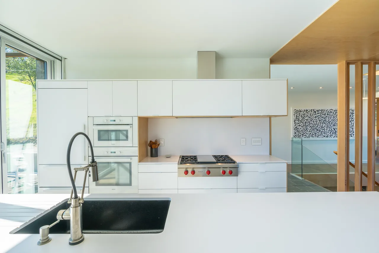 A modern kitchen featuring white built-in cabinetry, gas cooktop, double ovens, and an undermount sink on a white countertop.