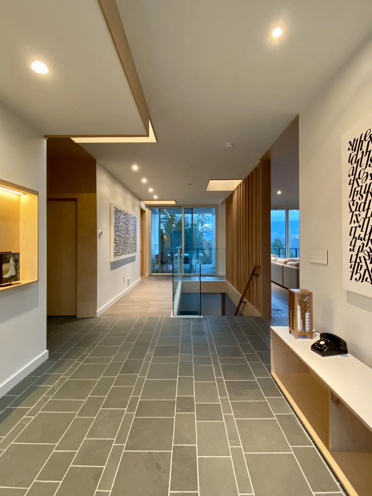 Modern hallway with tile flooring, wood accents, recessed lighting, and stairwell with wooden slats.