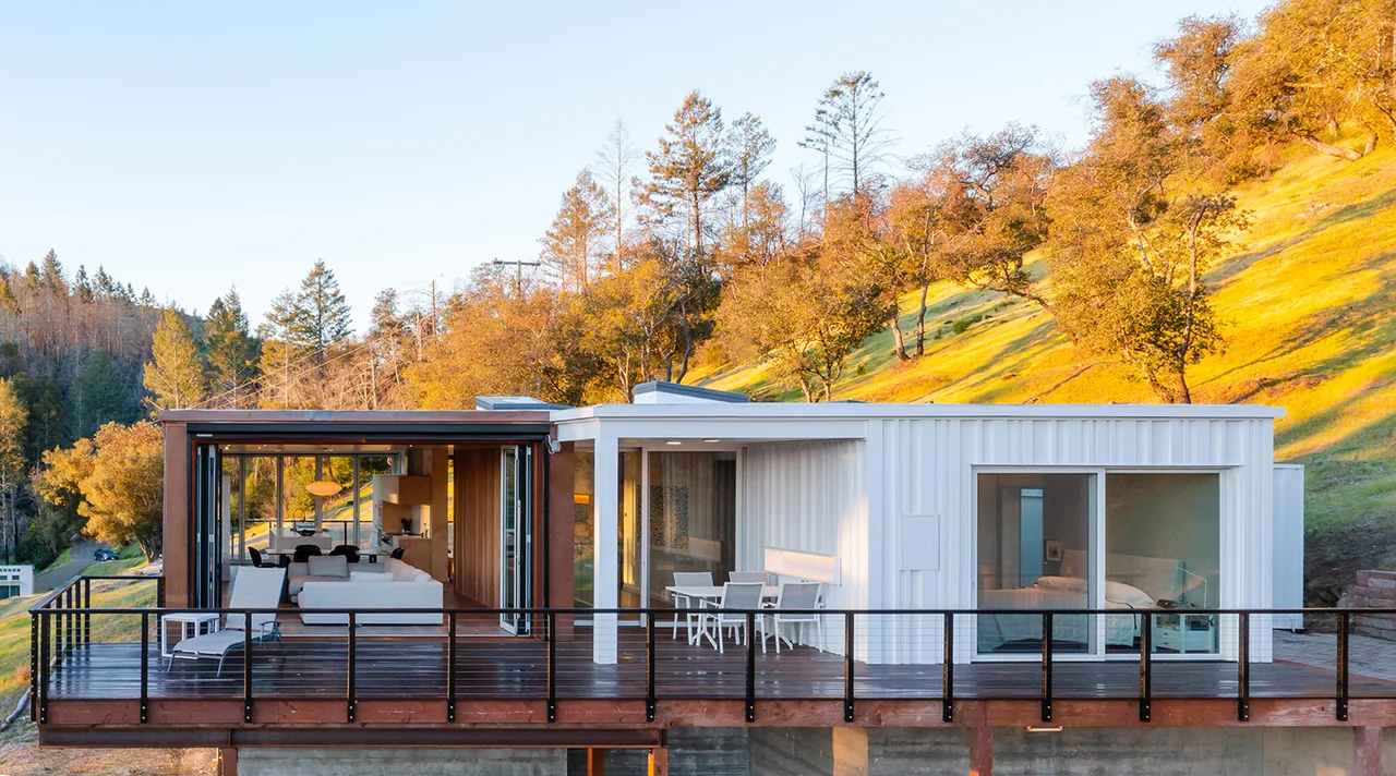 Exterior front view of a modern house with metal siding and large sliding glass doors opening onto a wooden deck.